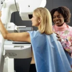 smiling woman standing near another woman beside mammogram machine