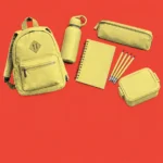 School supplies with a yellow lunchbox arranged on a coral background
